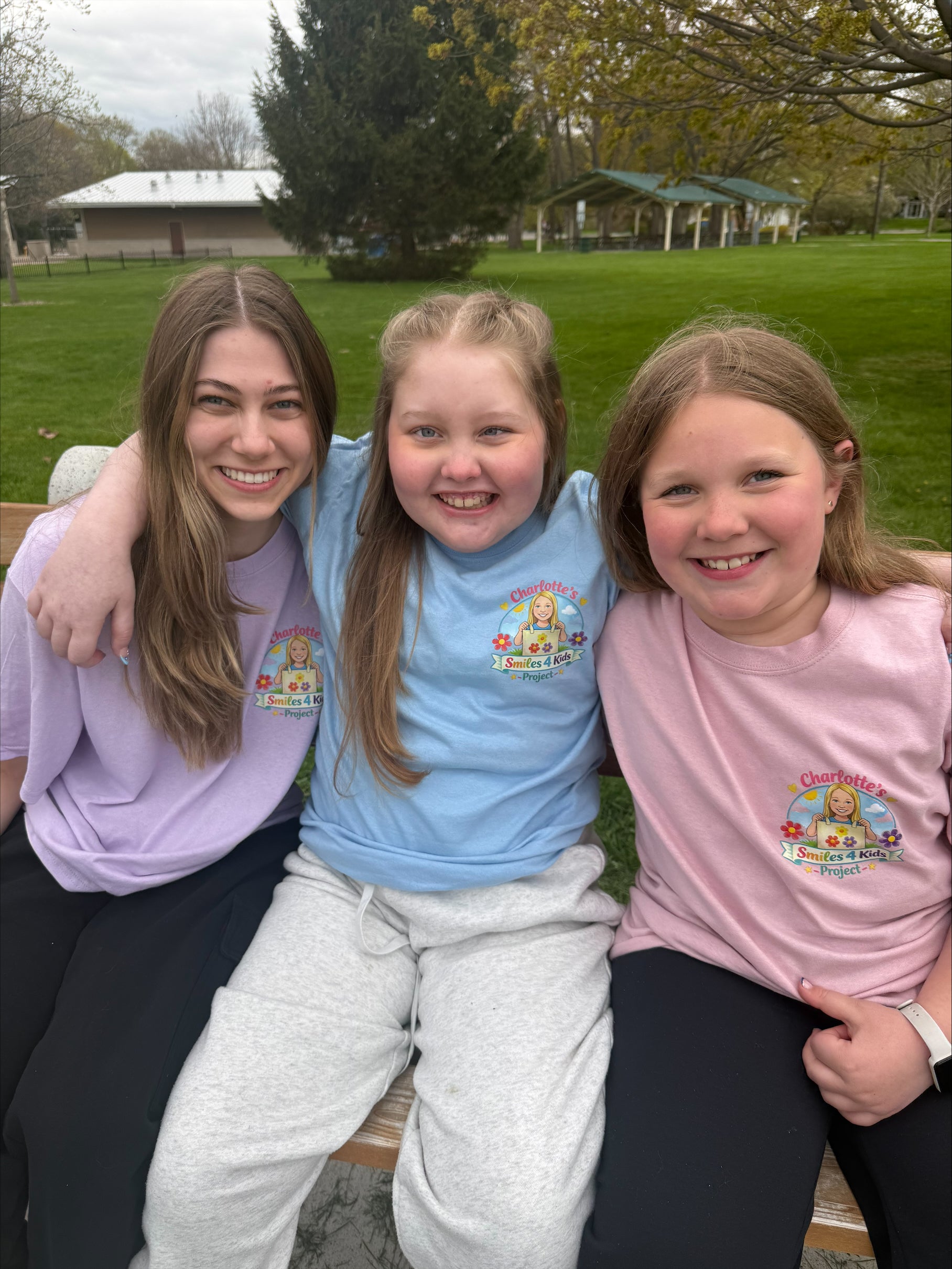 Three people sitting together in a park, wearing matching t-shirts with a colorful design.